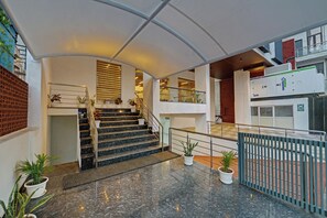 Um hall de hotel moderno com escadaria de mármore, plantas em vasos e guarda-corpo de vidro.