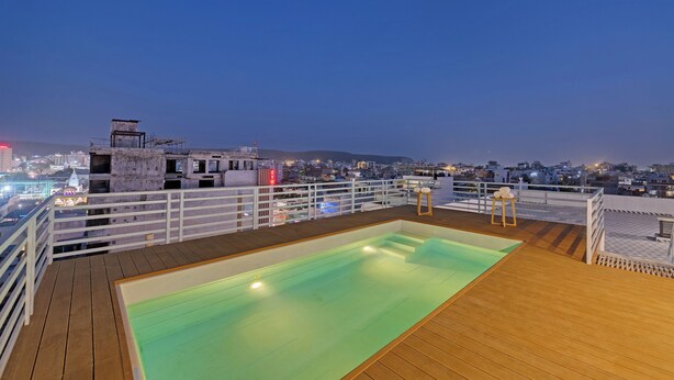 A rooftop pool with a wooden deck and white railings, overlooking a cityscape at dusk. - Click Collection Aster Jaipur  Raja Park (Jaipur)