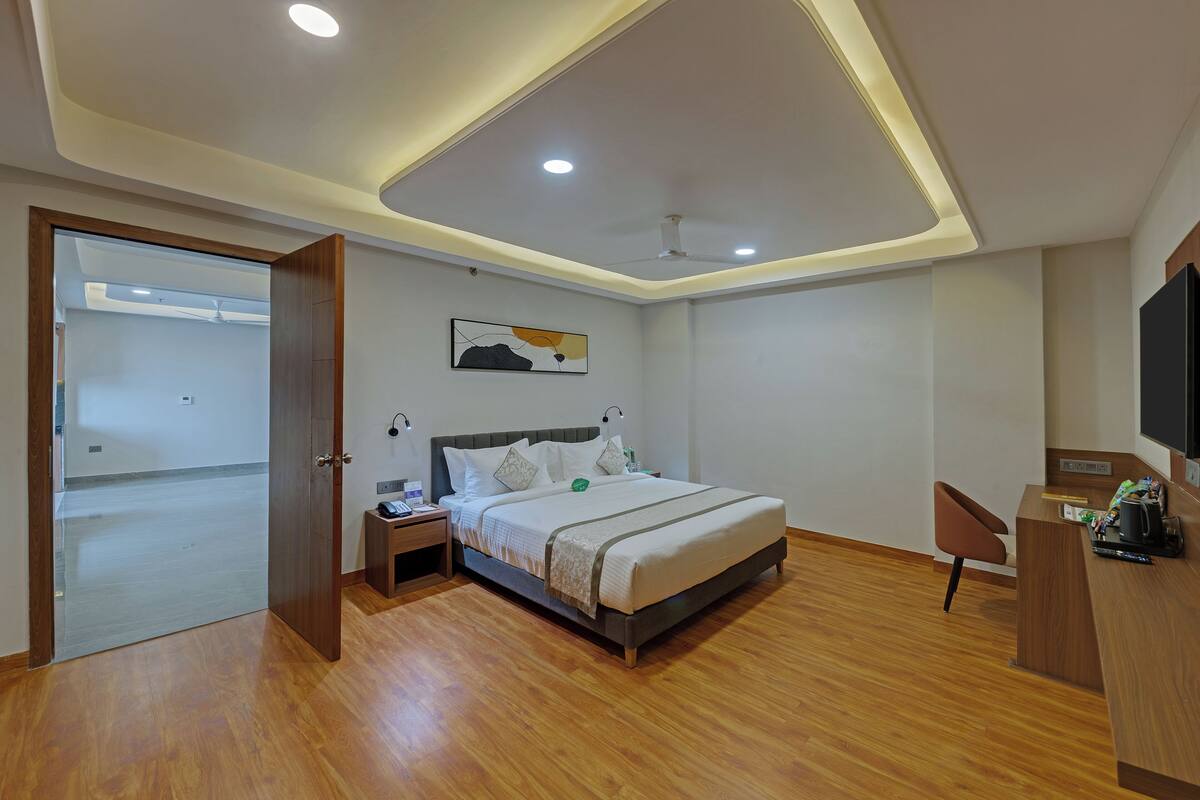 A modern hotel room with a wooden floor, a bed with white bedding, a desk with a chair, and a ceiling fan.