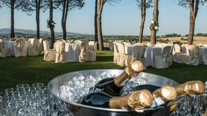 An outdoor event with tables set up on grass, surrounded by trees, and a view of distant hills.