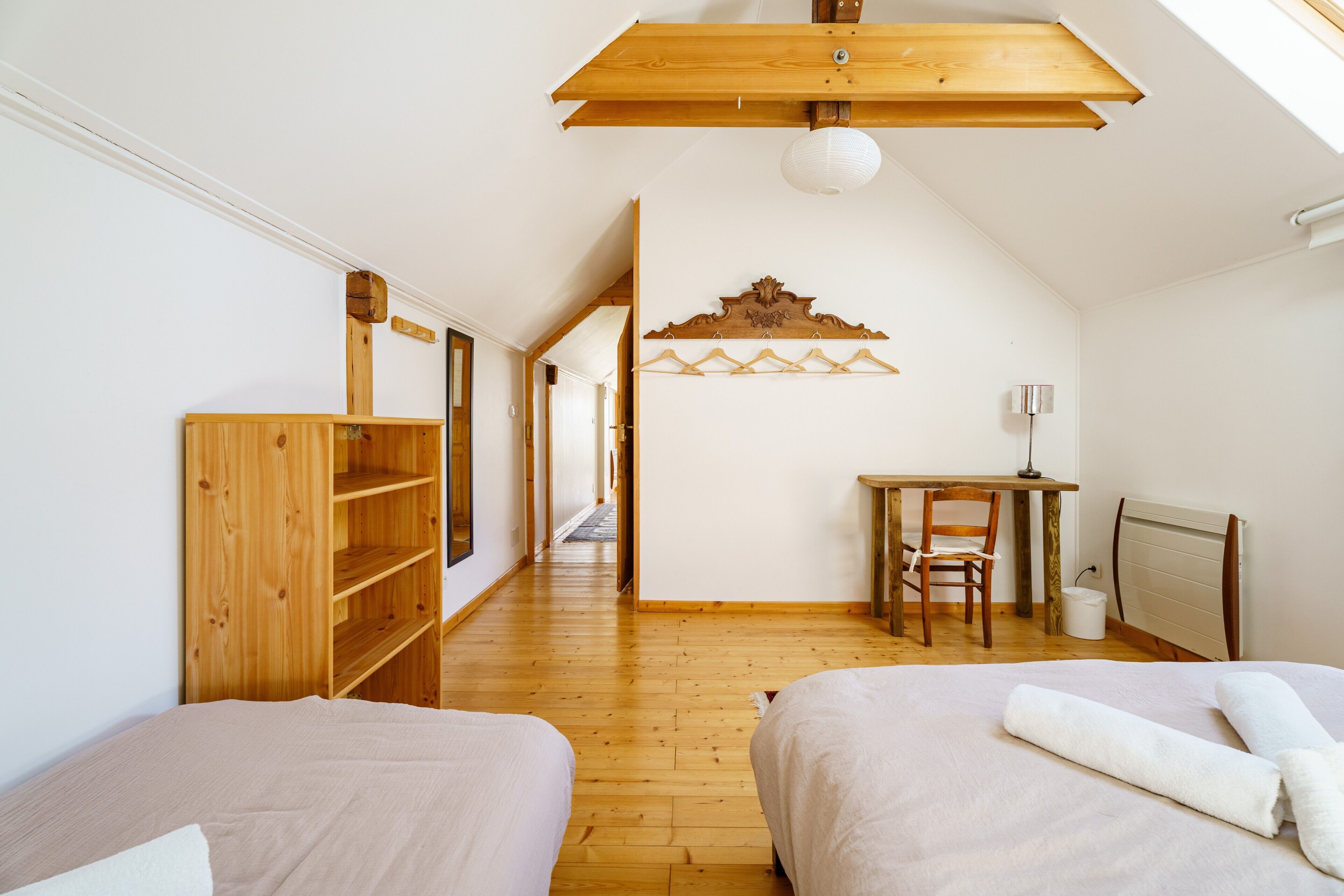 A bedroom with two beds, a wooden wardrobe, a desk with a chair, and a radiator.