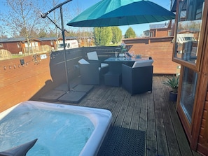 Un jacuzzi, mobiliario exterior y una terraza de madera con vistas a edificios circundantes.