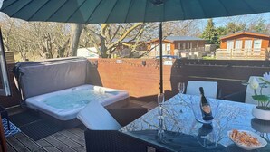 A hot tub, outdoor table with wine glasses, and a bowl of snacks under a large umbrella.