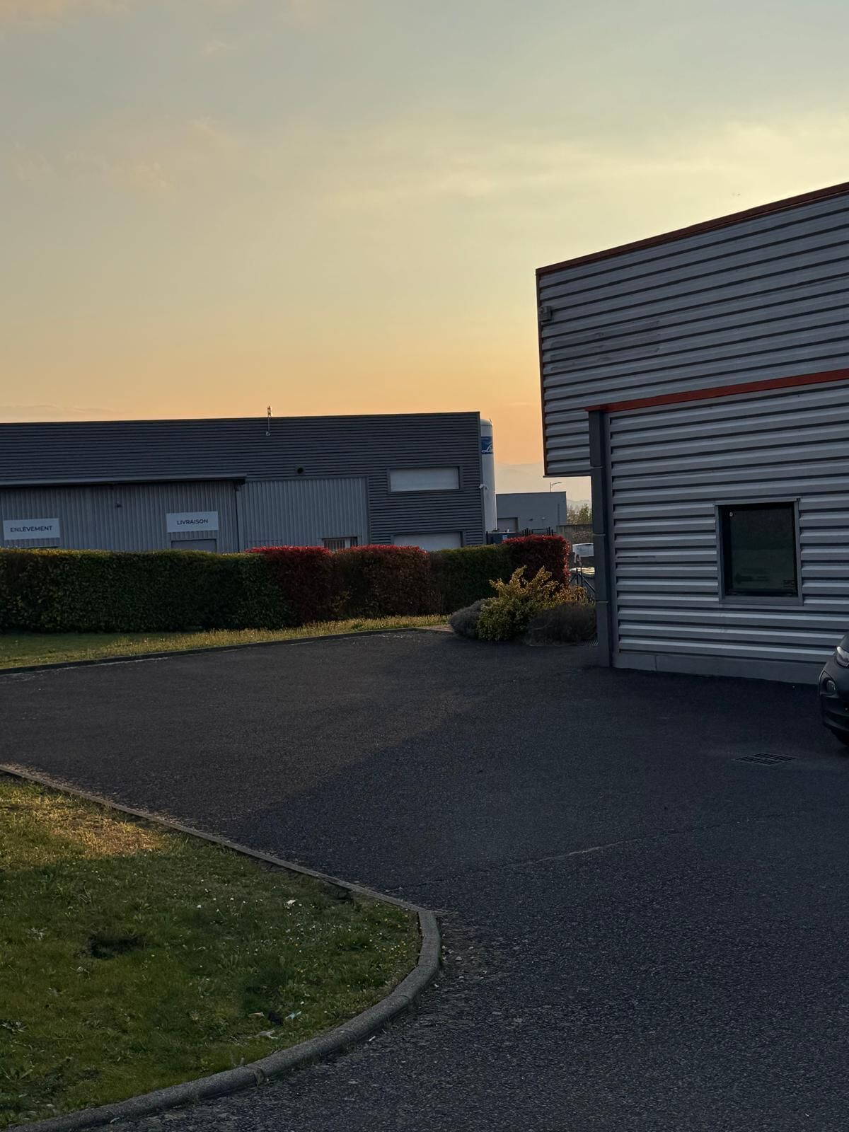 A modern industrial building with a paved driveway and a small parking area.