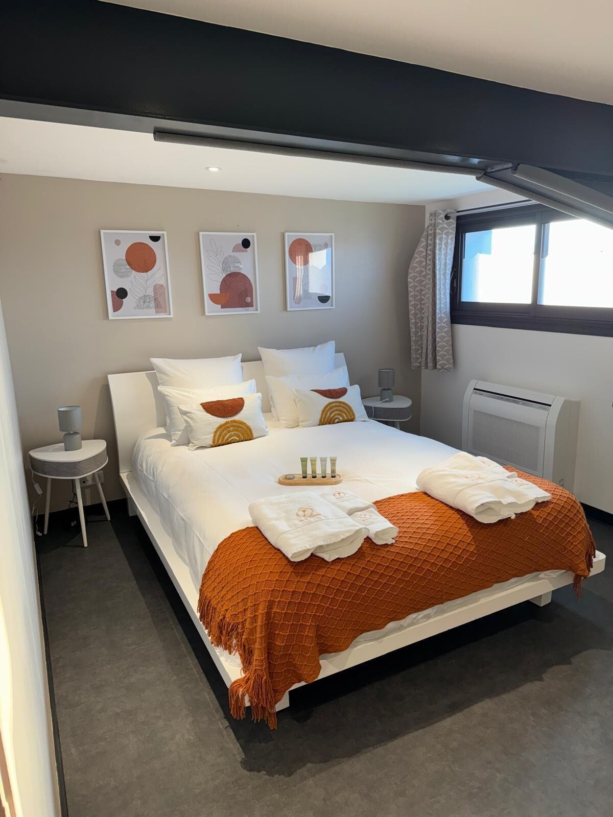 A modern hotel room with a large bed, bedside tables, wall art, and a window with curtains.