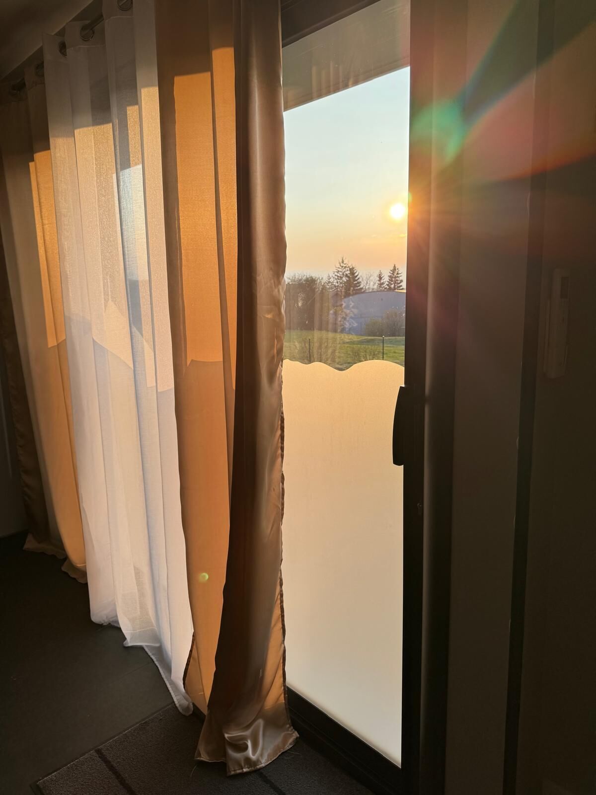 Una habitación con un ventanal grande, una puerta con panel de vidrio esmerilado y una cortina parcialmente recogida.