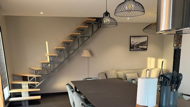 Una cocina moderna con una isla central, taburetes de bar, una escalera y un comedor.