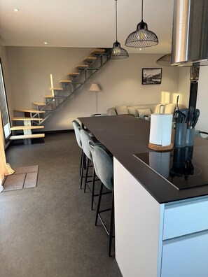 A modern kitchen with a central island, bar stools, a staircase, and a dining area. - Résidence du Champ Lamet (Pont-du-Château)
