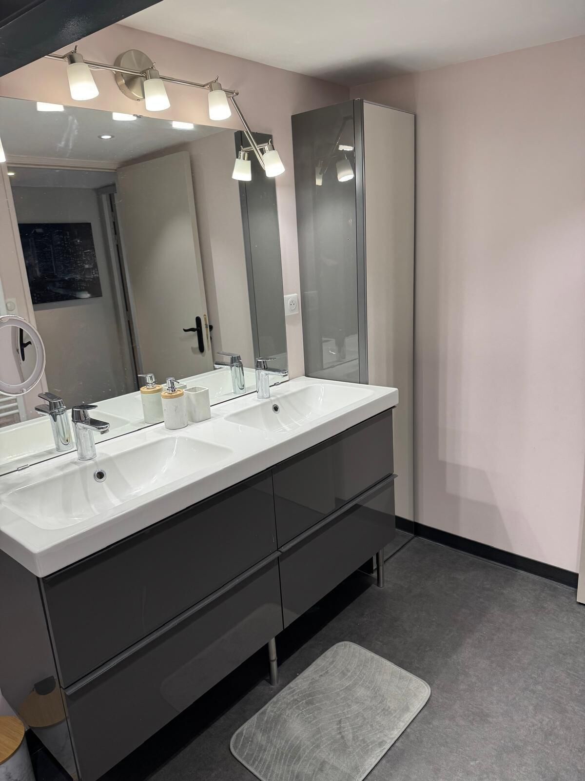 Een moderne badkamer met twee wastafels, een grote spiegel en verlichting in het plafond.