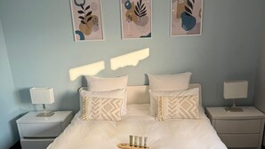 Una cama bien tendida con almohadas, una mesita de noche con lámpara, y decoración en la pared sobre la cama.