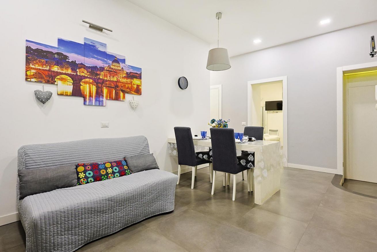 A modern living room with a grey sofa, a dining area with a white table and black chairs, and a large cityscape painting on the wall.