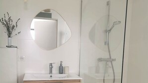 A modern bathroom with a glass shower enclosure, a wooden vanity, and a round mirror. - Vergisson room (Prissé)