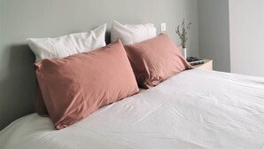 Een bed met witte en roze kussens, een nachtkastje met een lamp, en een wandlamp.