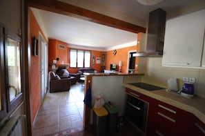Une cuisine équipée d’un évier, d’une cuisinière et de placards, un coin repas avec une table et des chaises, et un salon avec un canapé et un téléviseur.