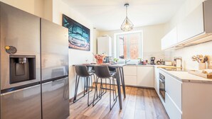 Een moderne keuken met een roestvrijstalen koelkast, een eethoek met twee stoelen, een koffiezetapparaat en een hanglamp.
