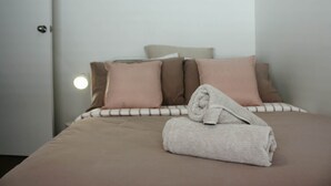 Una cama bien hecha con una toalla doblada, una lámpara de noche y una puerta con luz redonda.