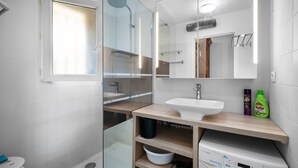 A modern bathroom with a glass shower enclosure, a white sink, and a built-in washing machine. - Beautiful 2-Bedroom Apartment in Green Estate with Shared Pool, Balcony & Wi-Fi (Six-Fours-les-Plages)