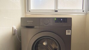 Une machine à laver à chargement frontal, située dans une buanderie avec une fenêtre au-dessus.