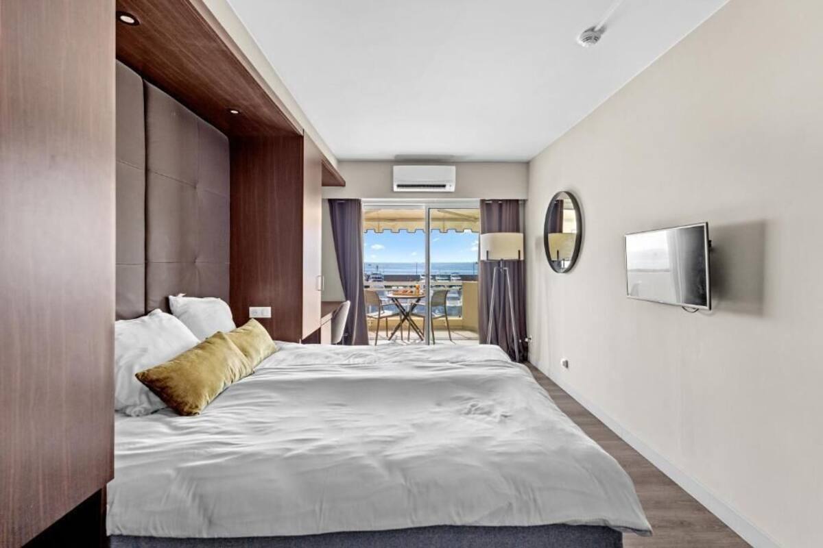 A hotel room with a bed, a TV, a balcony with a table and chairs, and an air conditioning unit.