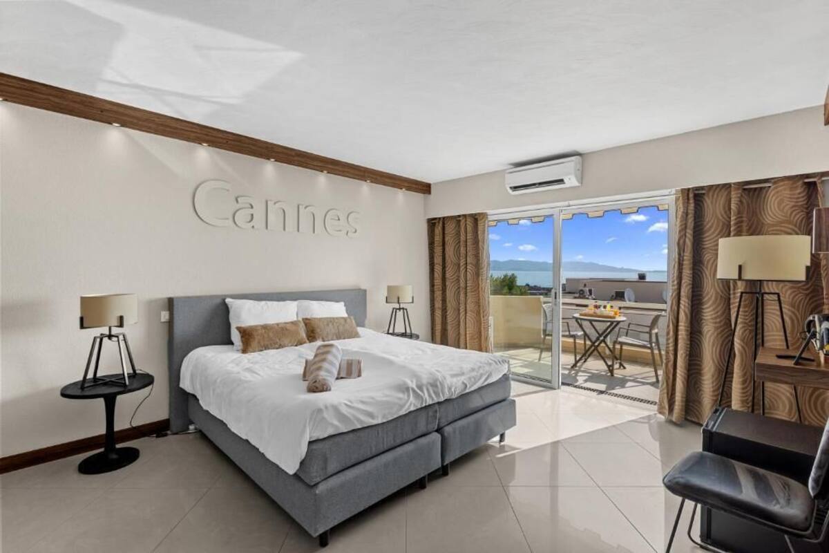 A hotel room with a bed, a desk, a chair, a lamp, and a view of the outdoors.