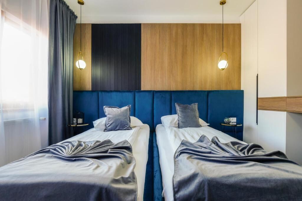 Habitación de hotel con dos camas, un cabecero de madera, una pared azul decorativa y mesitas de noche con lámparas.
