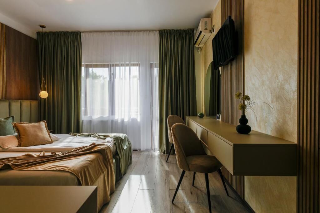Une chambre d’hôtel avec un lit, un bureau, une chaise, une télévision et une fenêtre avec des rideaux.