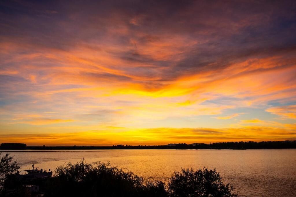 Un coucher de soleil sur une étendue d’eau, avec une silhouette de terre visible au loin.