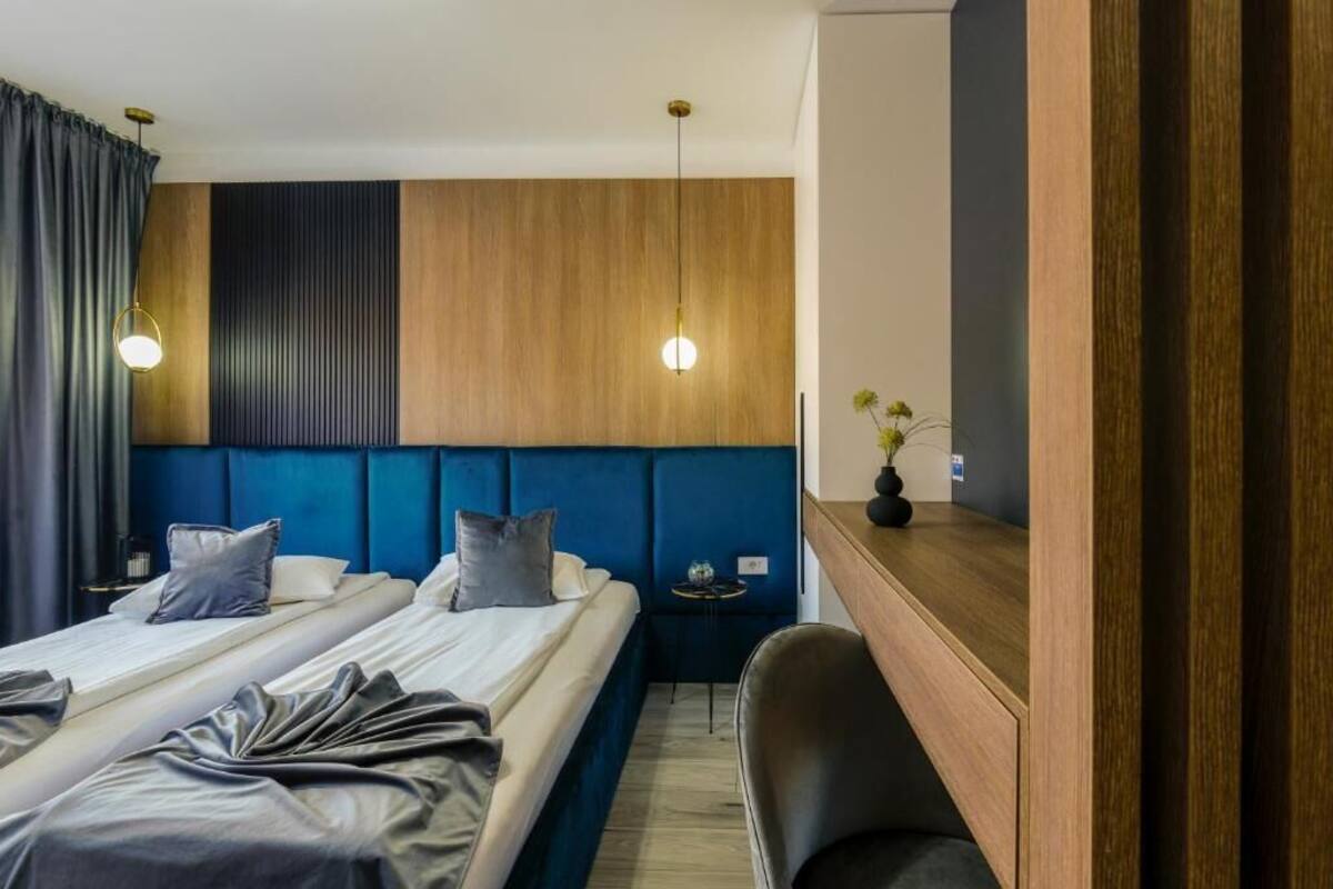 Ein Hotelzimmer mit zwei Betten, einem Holzkopfteil, einem kleinen Tisch, einem Stuhl und einem Nachttisch.
