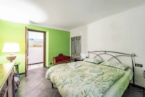 Ein Schlafzimmer mit einem Bett, einem Nachttisch, einer Lampe, einem roten Sessel und einer Tür zu einem weiteren Raum.