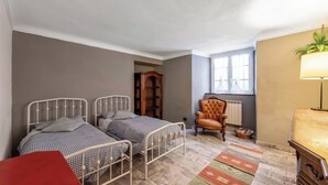 A bedroom with two metal beds, a red chair, a wooden cabinet, a lamp, and a window. - Genova House Via Caffaro (Genoa)