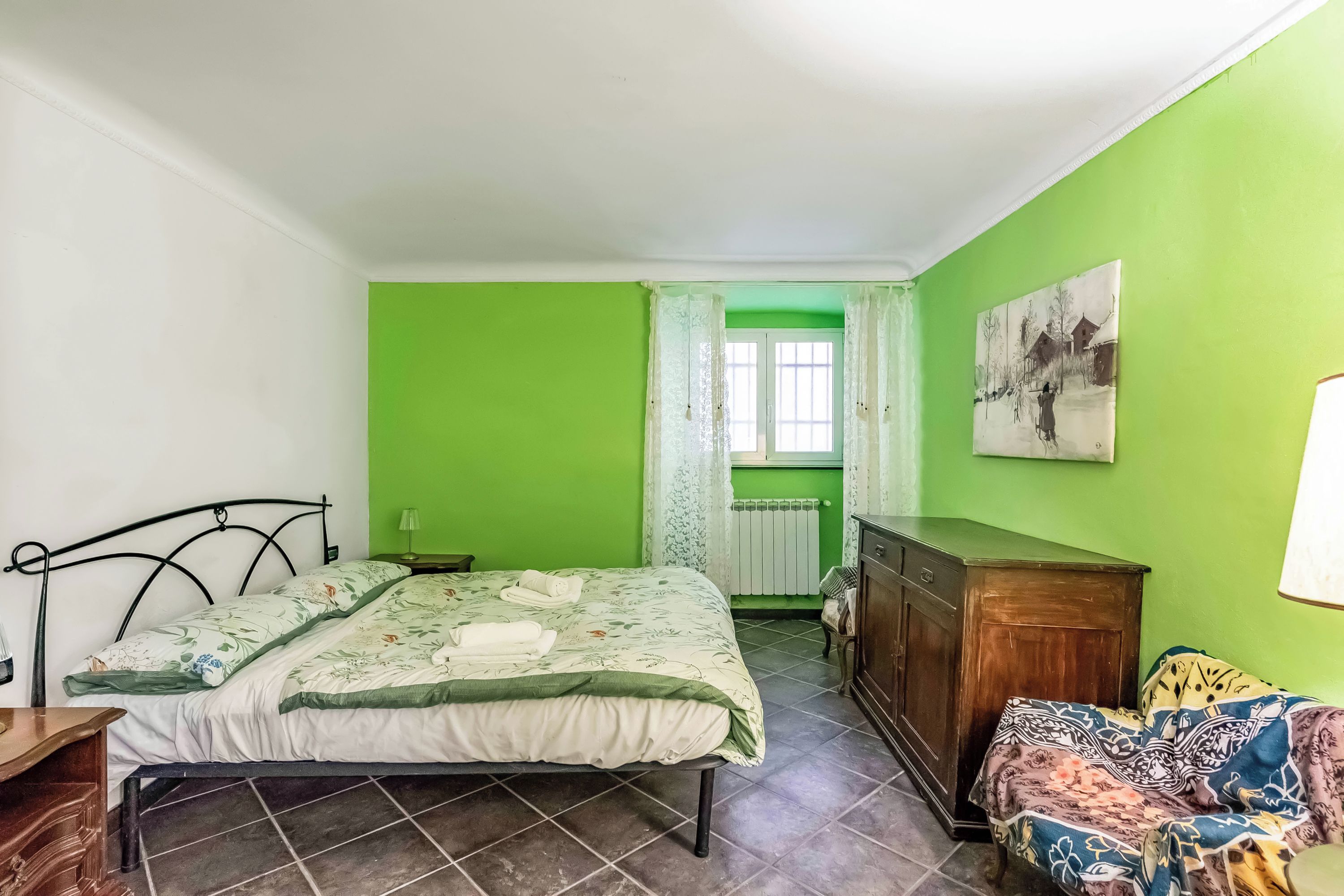 A bedroom with a bed, a dresser, a radiator, and a window with curtains.