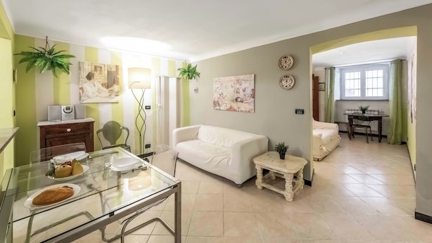 A living room with a white sofa, a glass dining table with plates, a small table with a lamp, and a plant. - Genova House Via Caffaro (Genoa)