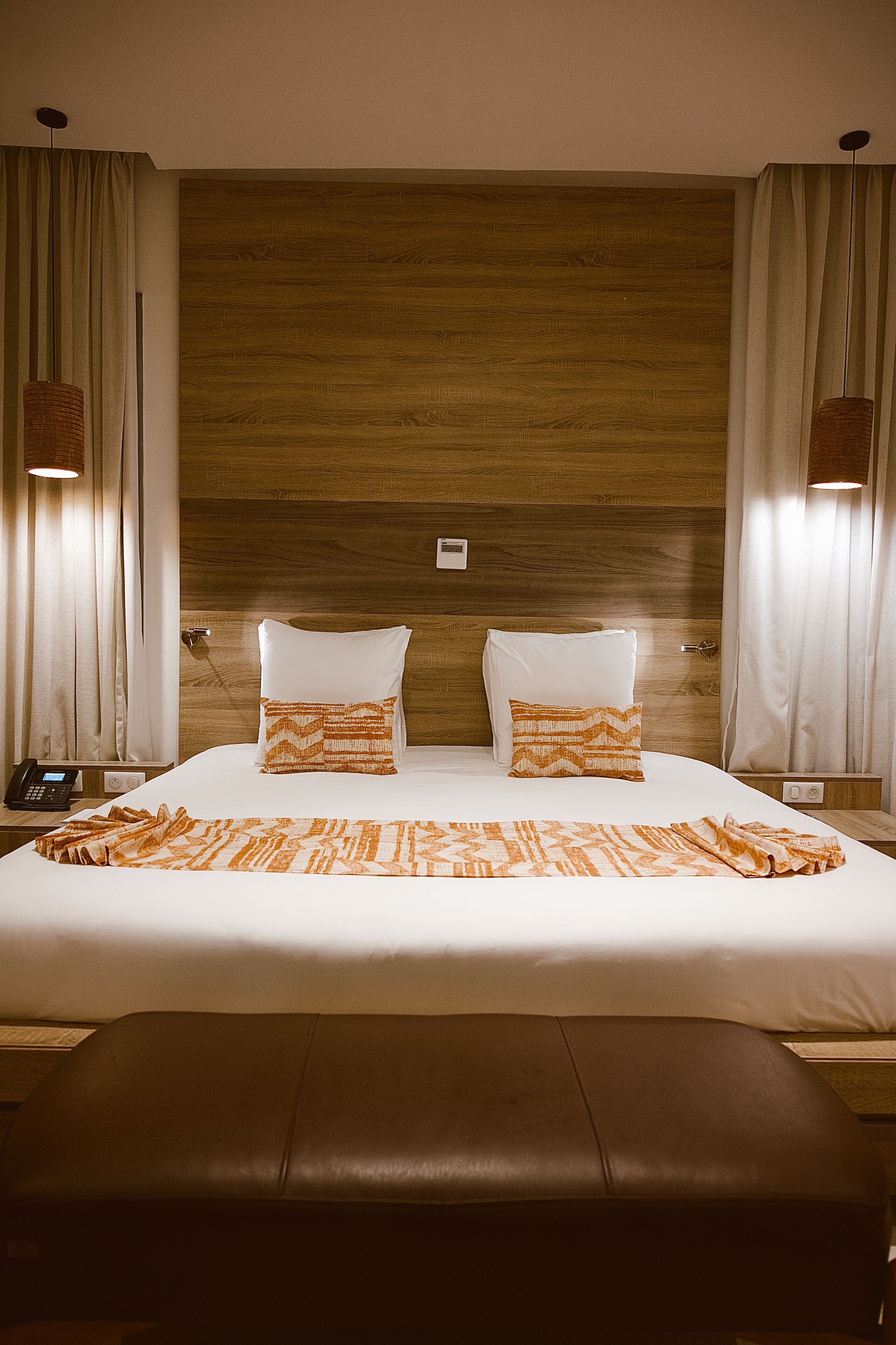 A hotel room with a large bed, two pillows, a bedside table with a phone, and a wall-mounted light fixture.