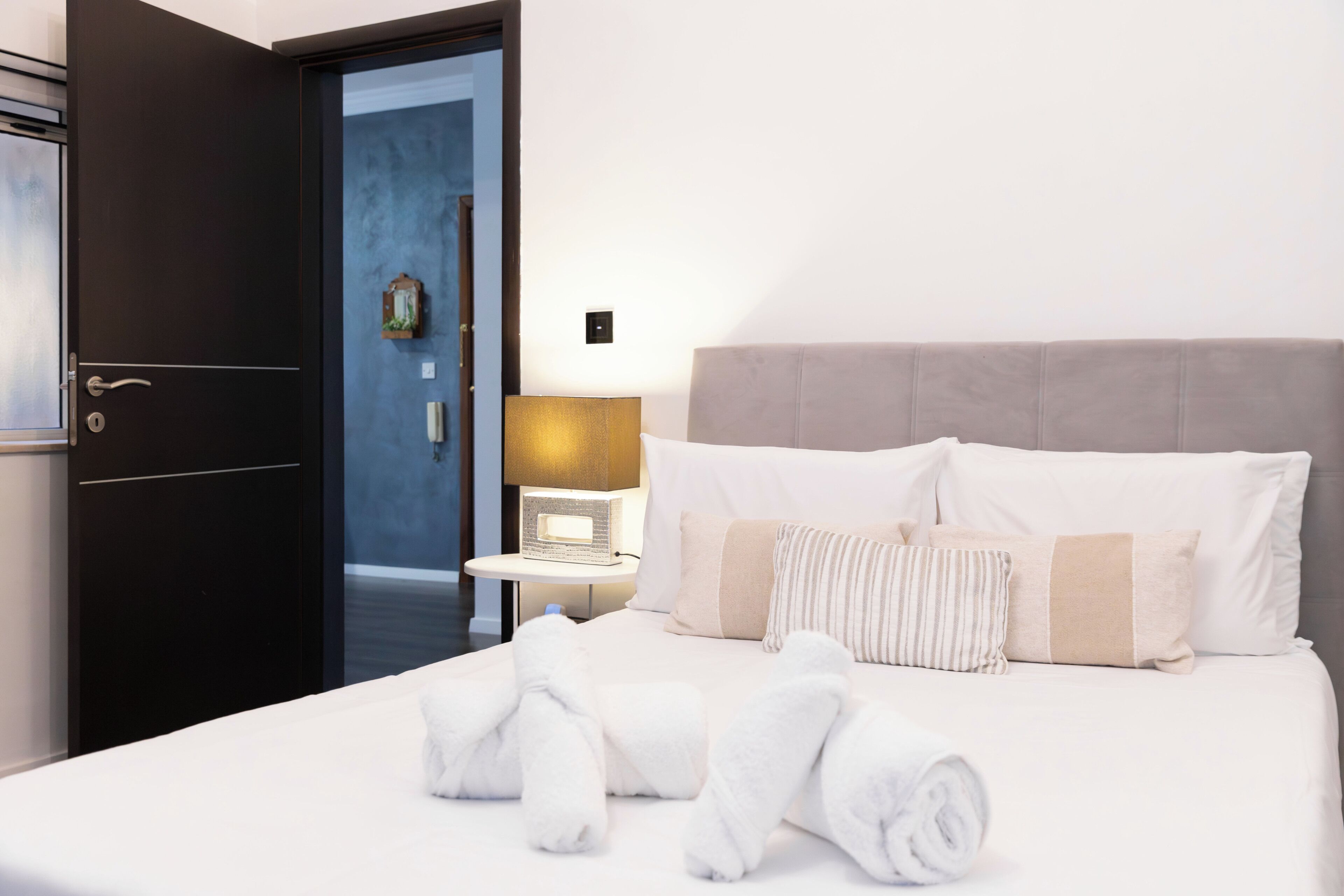 A hotel room with a bed, a nightstand, a lamp, and a door.