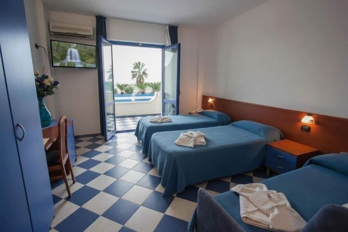 Ein Hotelzimmer mit zwei Betten, einem Fernseher, einem Schreibtisch und Blick auf einen Pool.