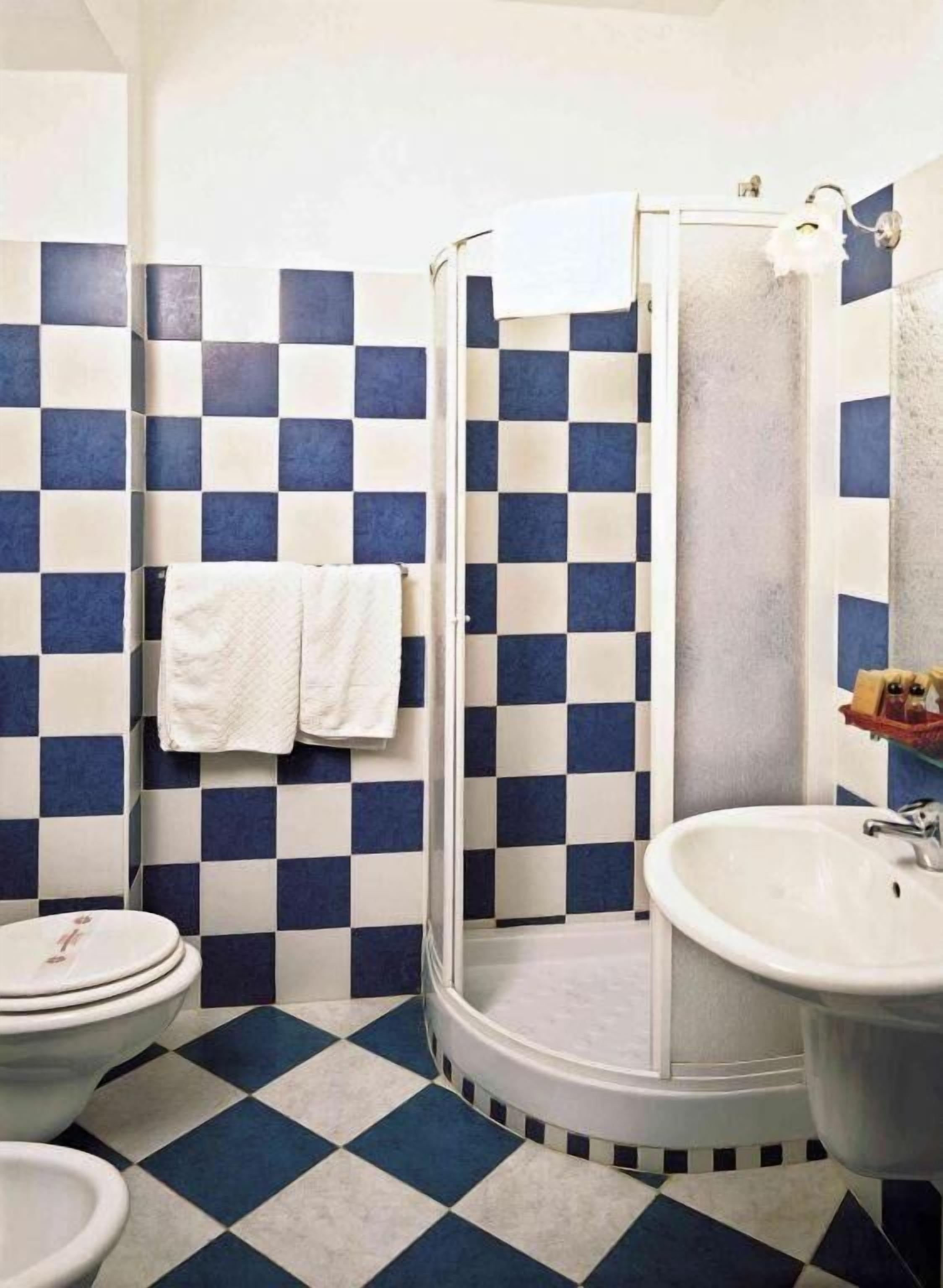 A bathroom with a checkered floor and walls, a white sink, a toilet, and a shower enclosure.