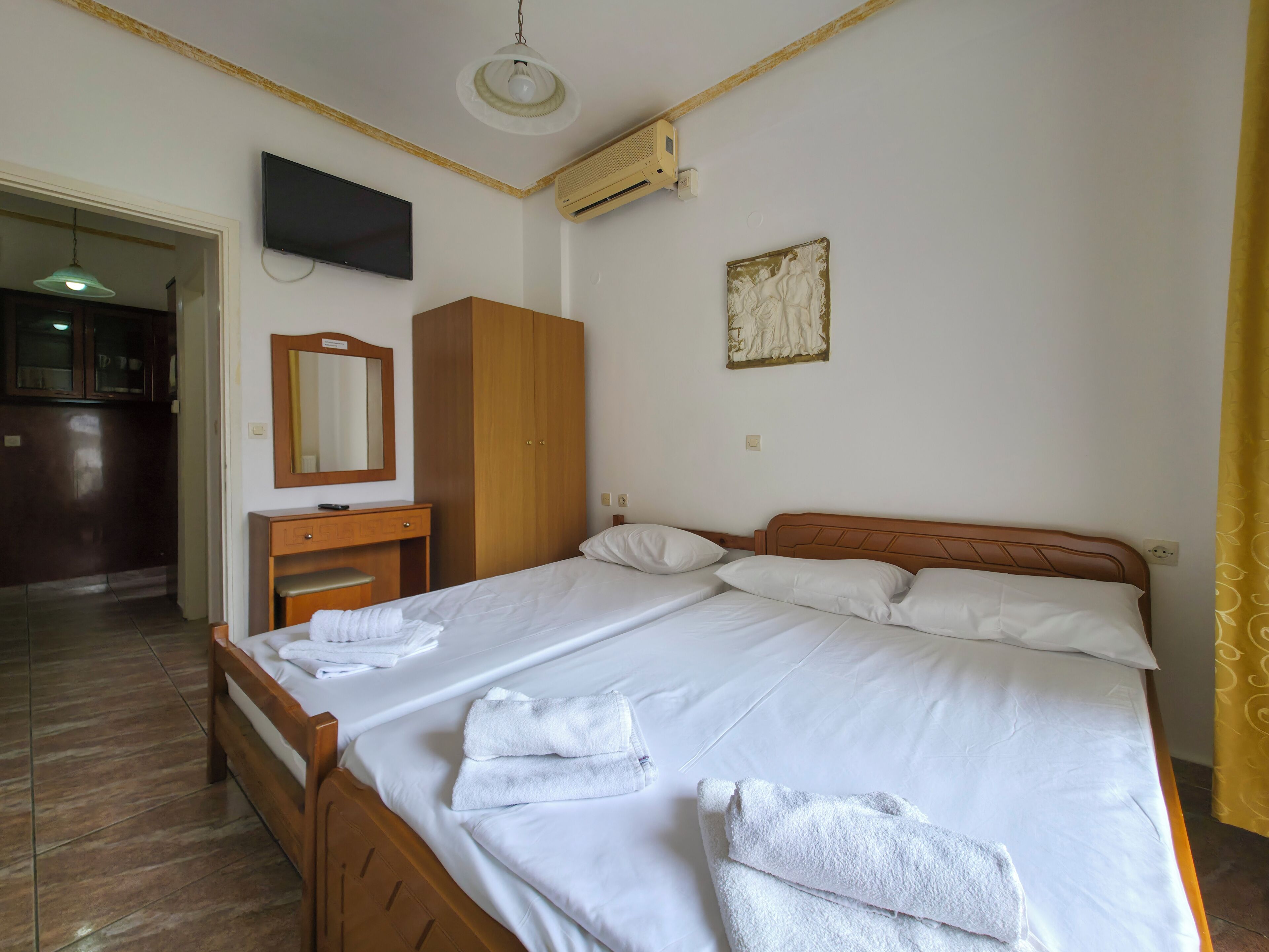 Una camera d'albergo con un letto, un armadio in legno, una scrivania con specchio e un televisore a parete.