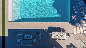 A rectangular swimming pool with clear water, surrounded by a stone border and a tiled deck area with outdoor seating. - Villa PinkBirdie de Luxe. Frontline Golf Las Colinas Piscine Rooftop Bali Lounge (Dehesa de Campoamor)
