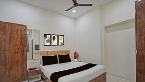 A bedroom with a bed, wooden wardrobe, bedside table, nightstand, ceiling fan, and wall-mounted artwork.