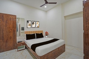 A bedroom with a bed, wooden wardrobe, bedside table, nightstand, ceiling fan, and wall-mounted artwork.