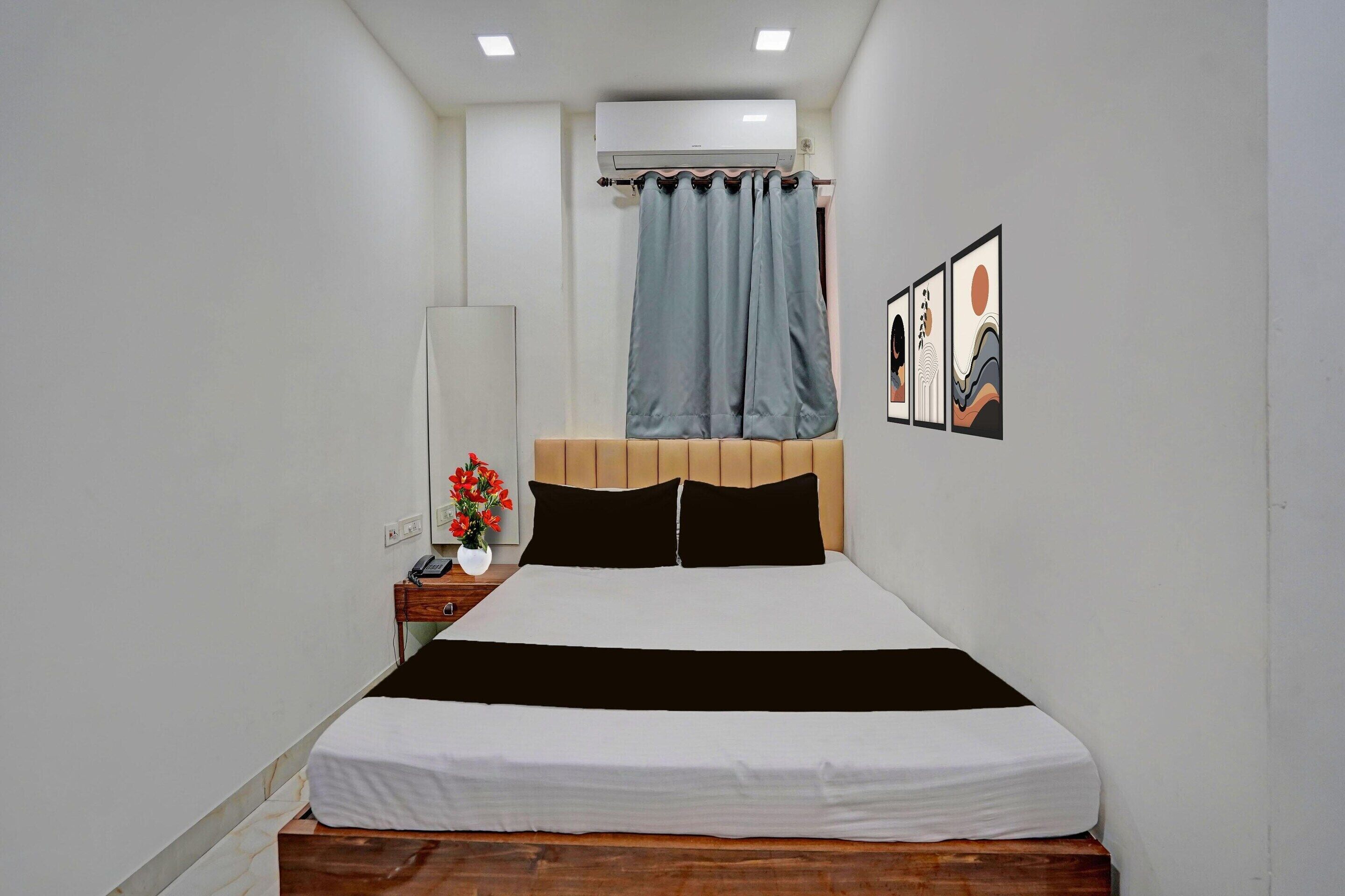 A bedroom with a bed, a nightstand, a mirror, a wall-mounted air conditioner, and a curtain.
