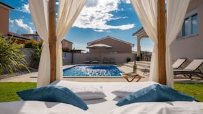 Ein Schlafzimmer am Pool mit Blick auf ein Schwimmbecken, Sitzgelegenheiten im Freien und einer überdachten Terrasse.