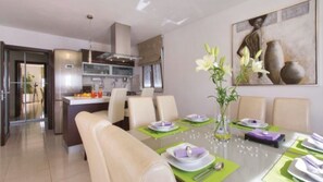 Een moderne eetruimte met een glazen tafel, groene placemats en witte stoelen.