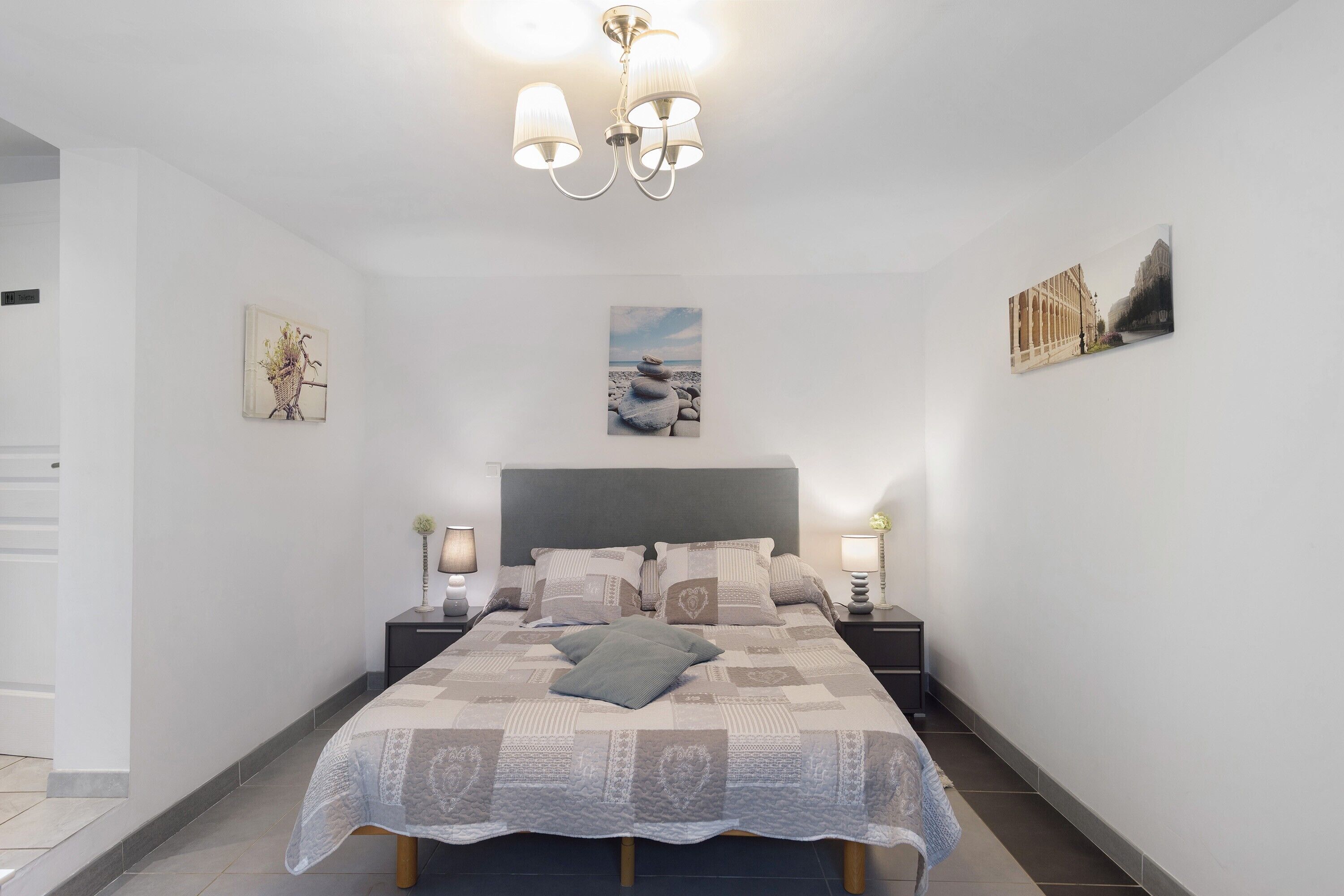 A bedroom with a bed, bedside tables, a chandelier, and wall art.