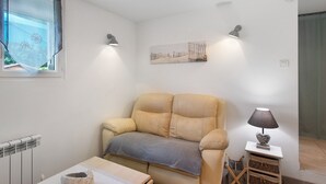 Un salon avec un canapé beige, une petite table, une lampe et un tableau accroché au mur.