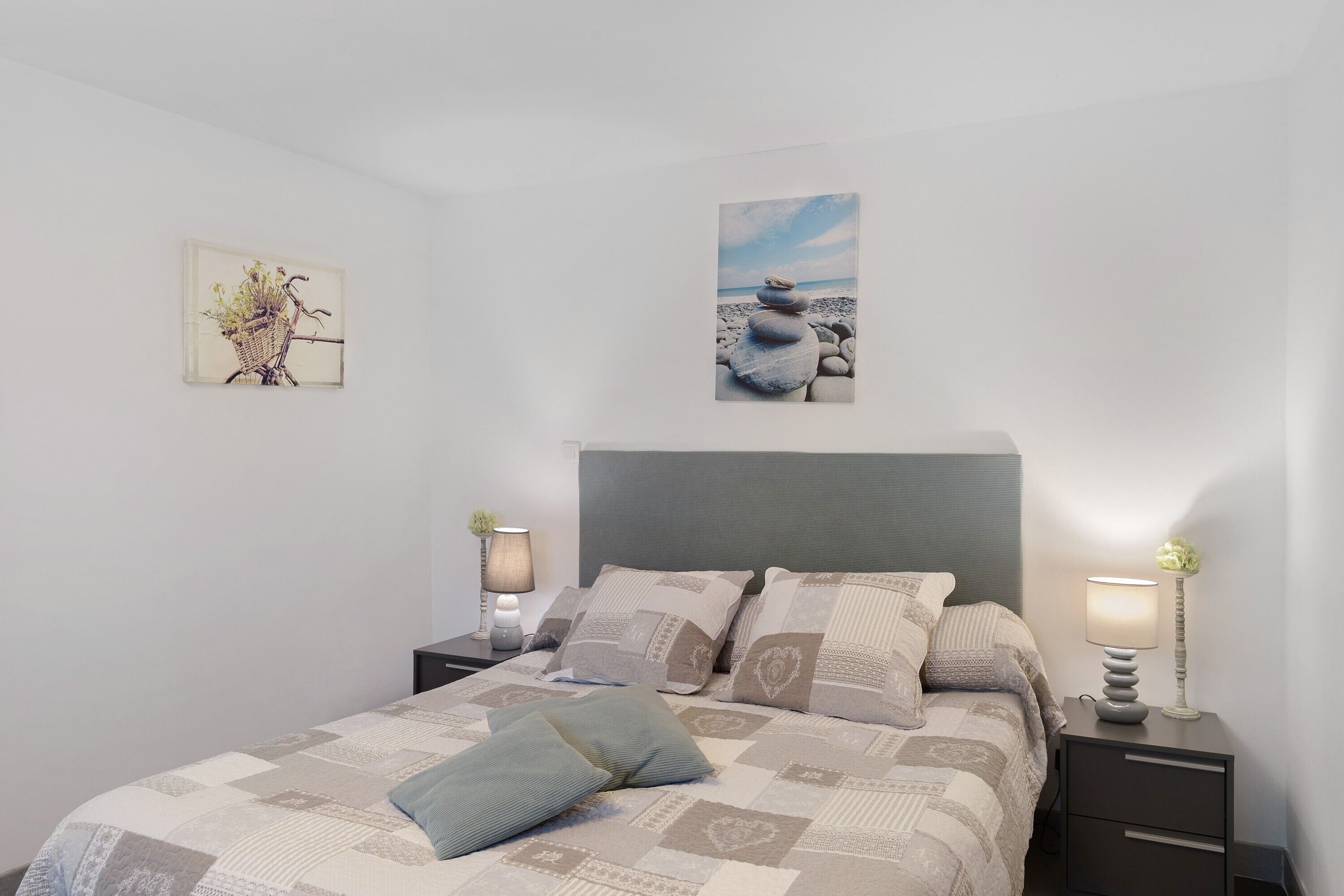 Ein Schlafzimmer mit einem Bett, zwei Nachttischen, einer Wandlampe und zwei gerahmten Bildern.