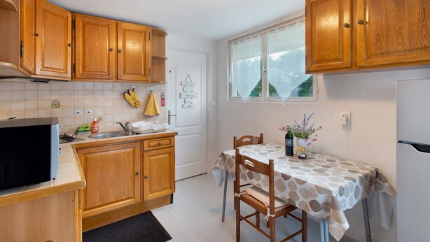 Une cuisine avec des meubles de rangement en bois, une table à manger recouverte d’une nappe à motifs et un réfrigérateur.