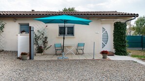 Une maison avec un patio, une table, deux chaises, un parasol et des plantes en pot.