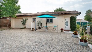 Un bâtiment d’un seul étage, doté d’un toit en tuiles, d’une allée en gravier et d’un patio aménagé avec une table et des chaises.