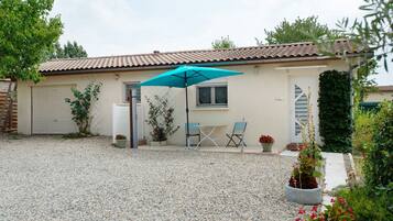 Une maison avec une allée en gravier, une terrasse avec une table et des chaises, et un parasol bleu.